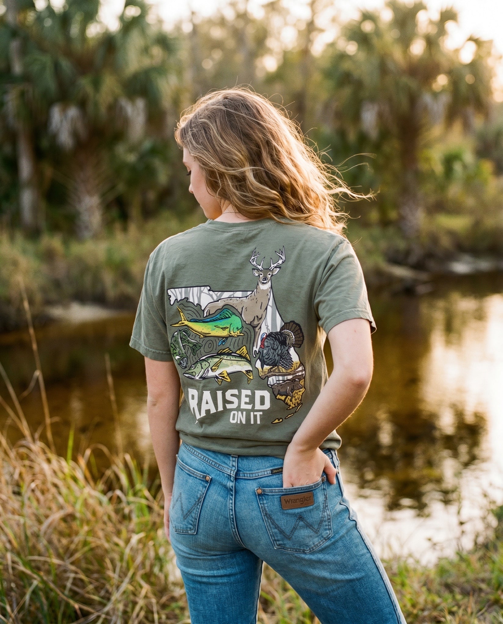 Woman wearing the olive Florida Sportsman Tee by a Florida creek, full back print visible