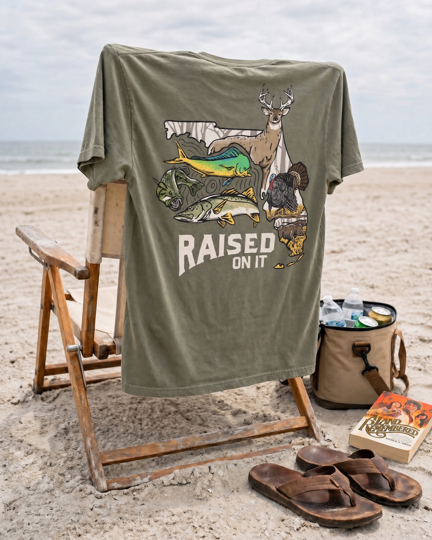 Olive Florida Sportsman Tee draped over a beach chair with a copy of A Land Remembered