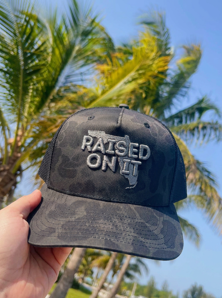 Silver Camo Florida Logo trucker hat held against palm trees
