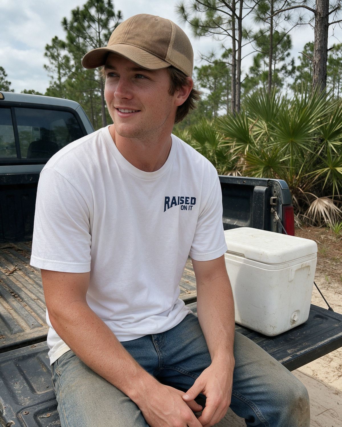 Man on a pickup tailgate wearing the Florida Cowboy tee, Raised On It chest logo