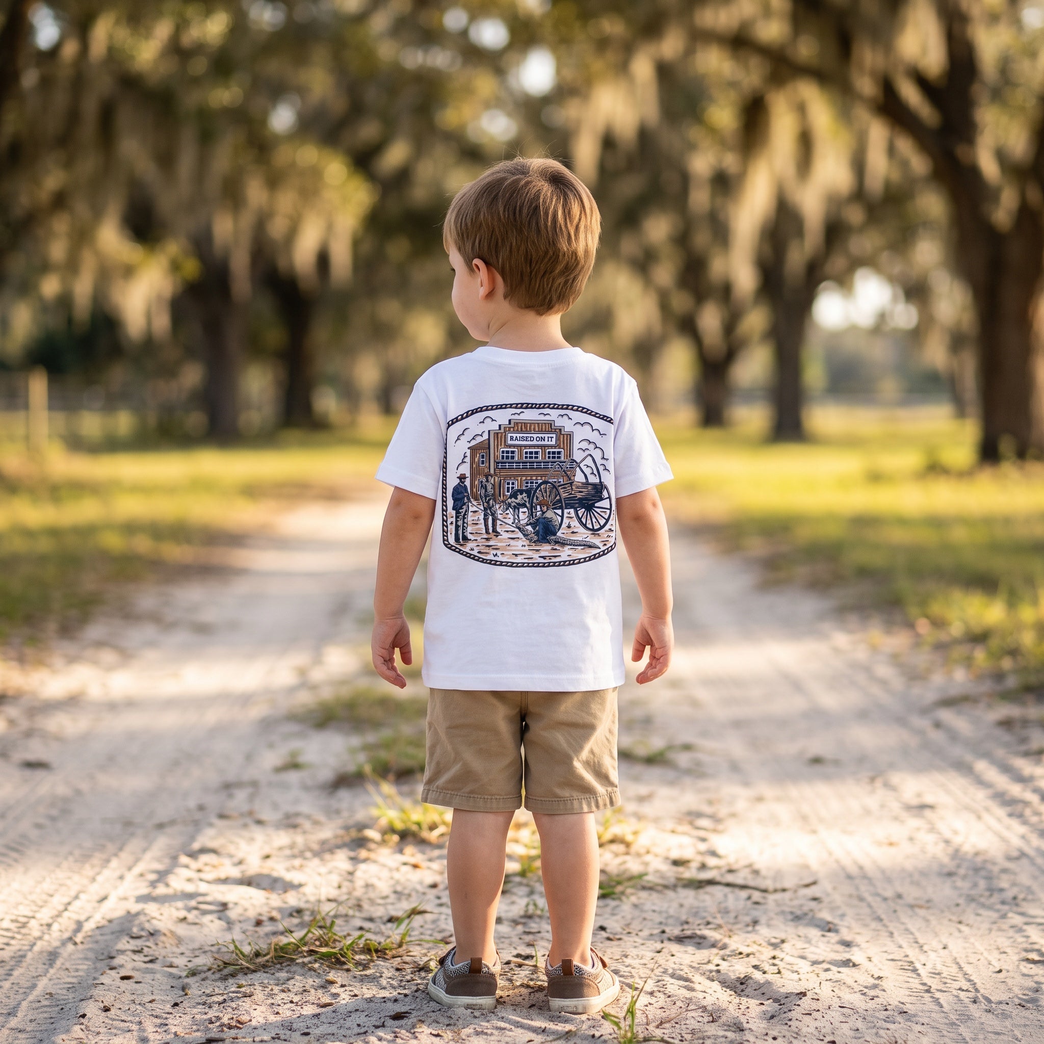 Toddler boy wearing the white Florida Cowboy Tee, back view of the full Raised On It ranch print