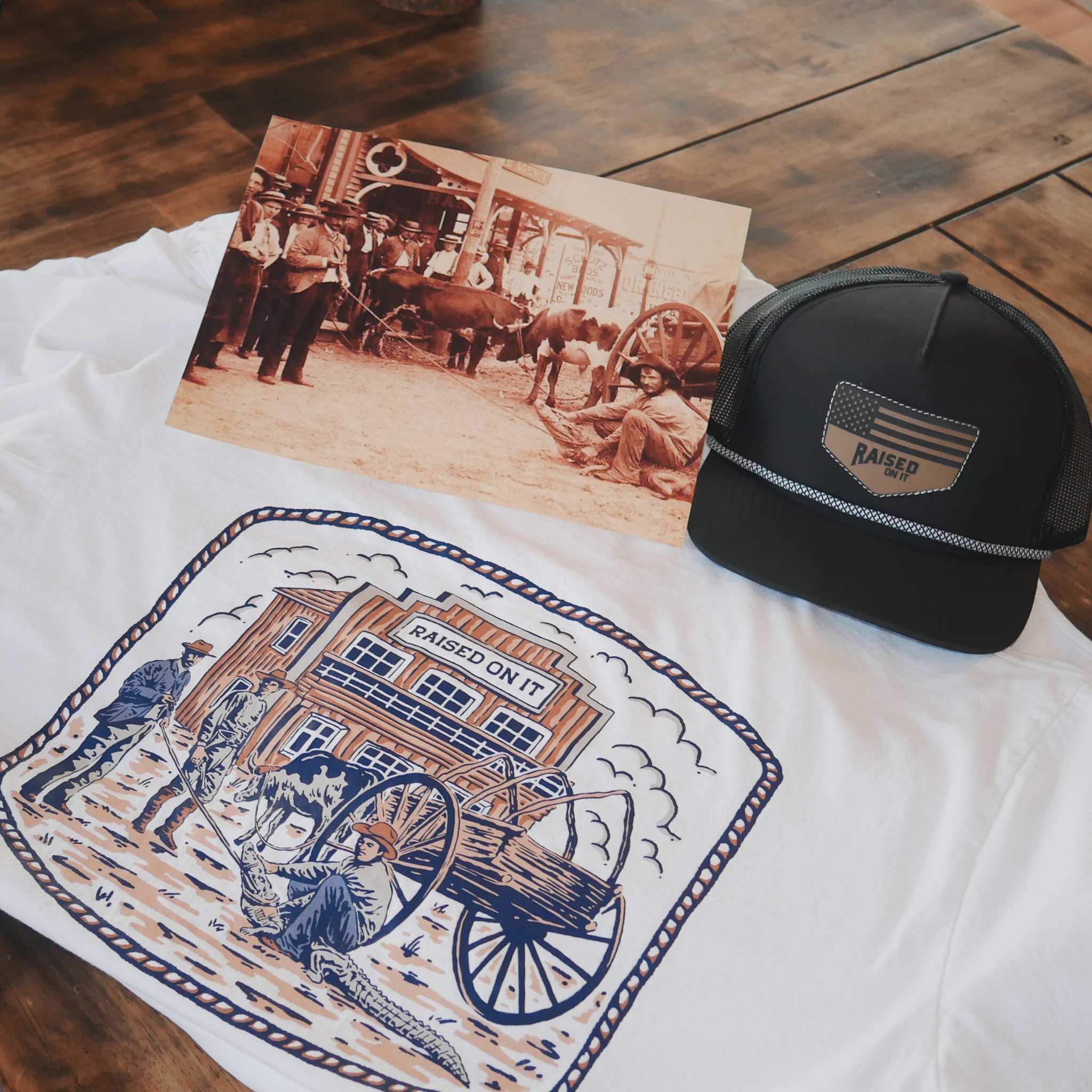 Florida Cowboy tee flat lay with a print of the original photograph and a Raised On It trucker hat