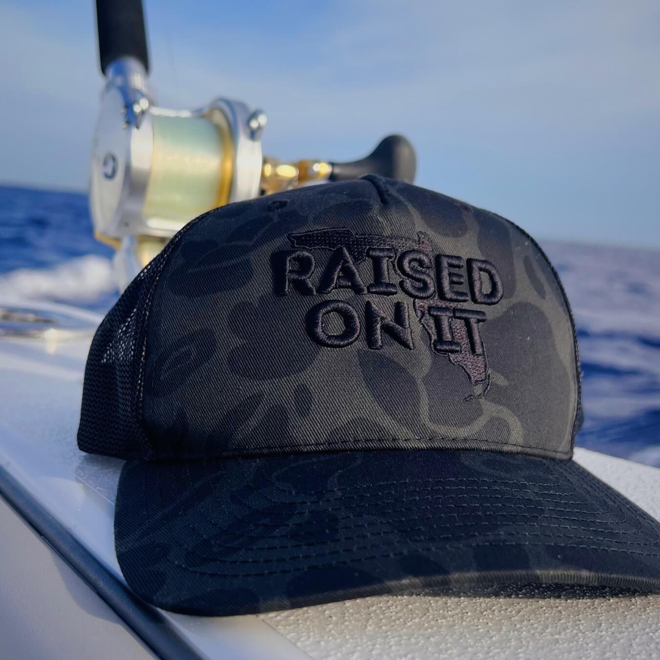 Subdued Camo Florida Logo trucker hat on a boat with offshore fishing reel